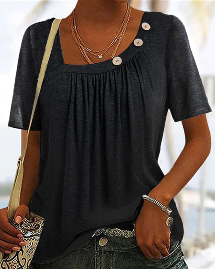 Front view, worn by model, of a comfortable grey short sleeve blouse with a square neckline and decorative buttons
