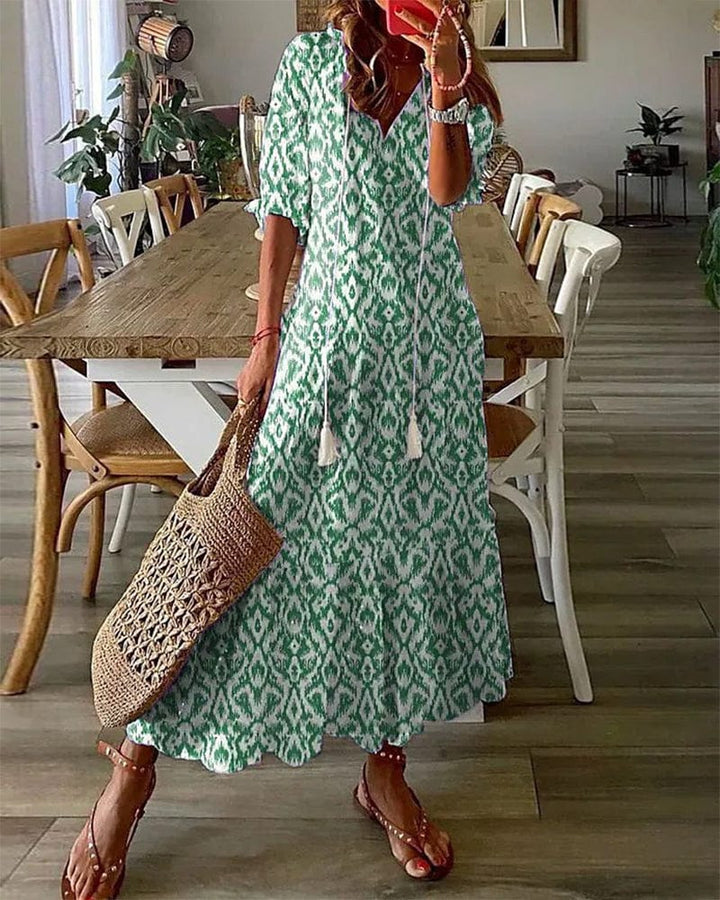 Front view of model wearing a green and white printed summer dress with a woven bag and sandals