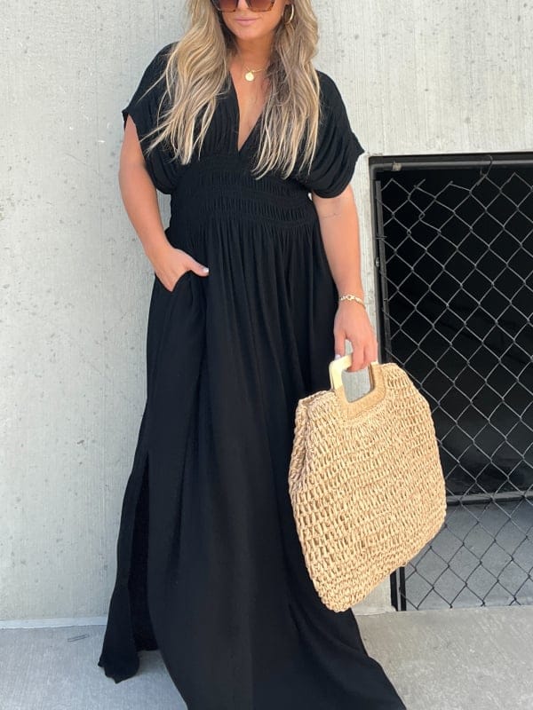 Front view of model wearing a black elegant summer maxi dress with pockets and a woven bag
