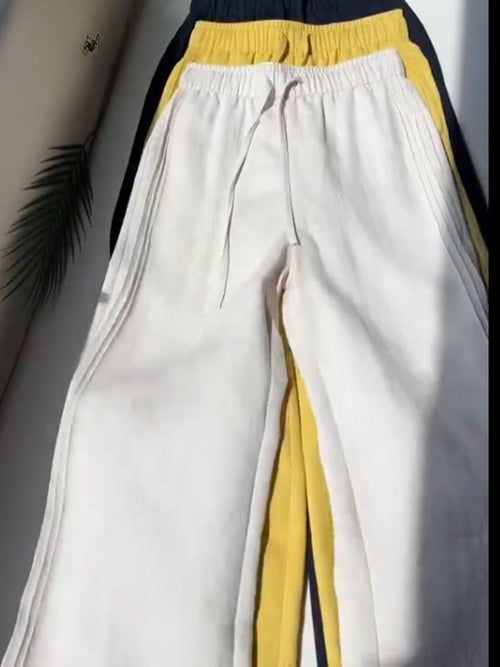 Flat lay of three pairs of Tencel linen wide leg casual pants in white, yellow, and navy with drawstrings