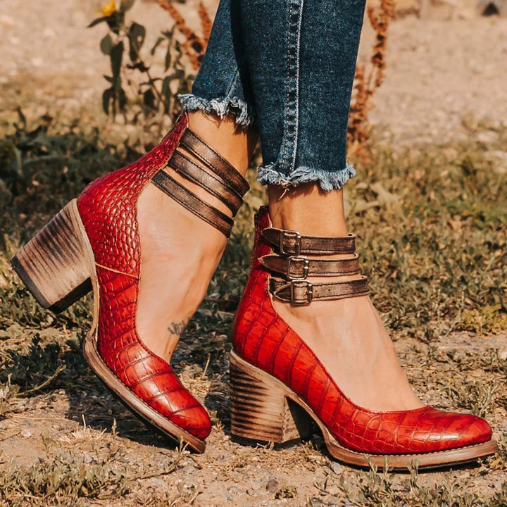 Worn by model, elegant vintage heeled sandals in red with triple buckled ankle straps and block heels on grass