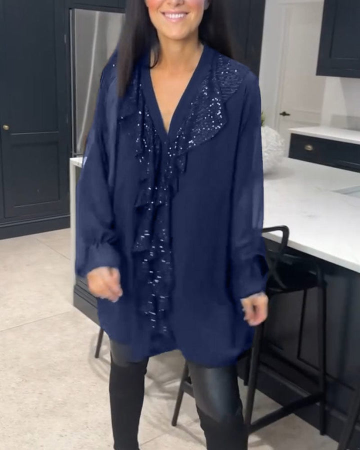 Front view of a woman wearing a navy ruffled blouse with sequin detail over black leather-look pants
