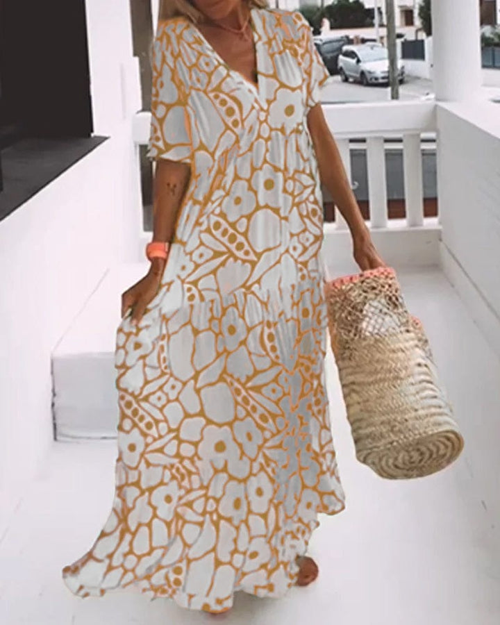 V neck printed maxi dress, three quarter view worn by model, holding a straw bag and walking on a balcony