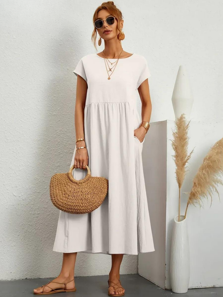 Front view, model wearing a white loose summer dress with short sleeves, sunglasses and a woven handbag