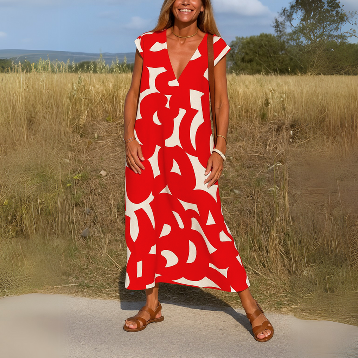 Front view of a woman wearing a red and white patterned flowing V-neck boho dress in a field