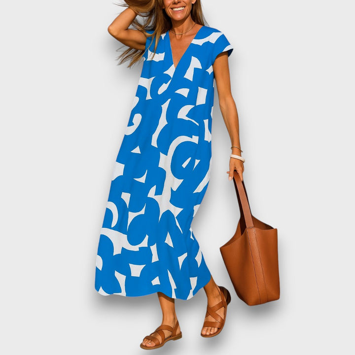 Front view, model wearing airy V-neck dress with blue and white abstract pattern, brown sandals and shoulder bag