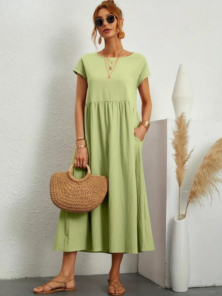 Front view, model wearing a light green loose summer dress with short sleeves and a woven handbag