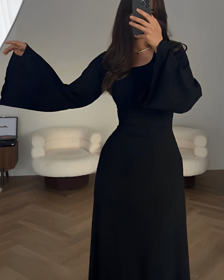 Front view of a model wearing a dark elegant knit maxi dress with a square neckline and flare sleeves