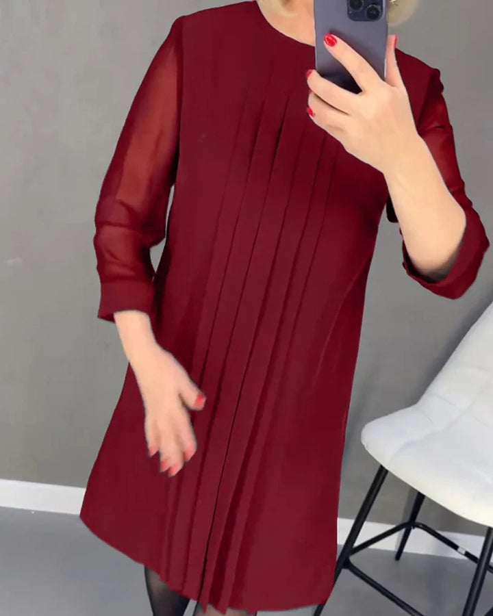 Front view, model in a dark red pleated knit dress with sheer sleeves, holding a phone to her chest