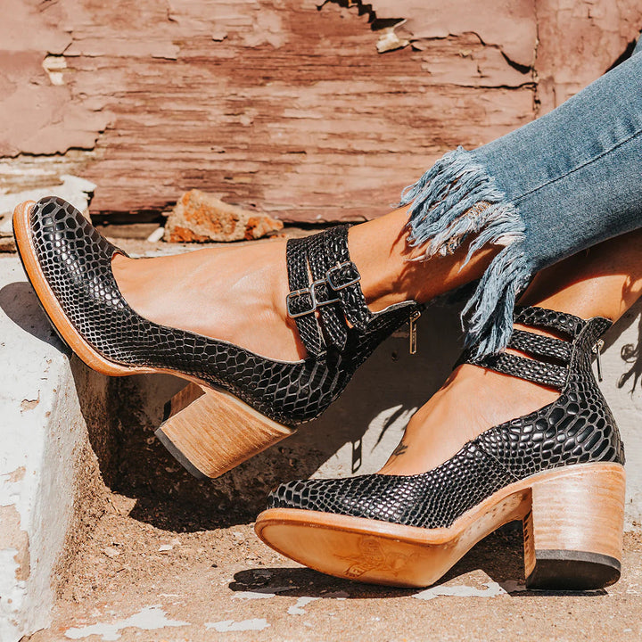Worn by model, close up of elegant vintage heeled sandals in black with triple buckled ankle straps