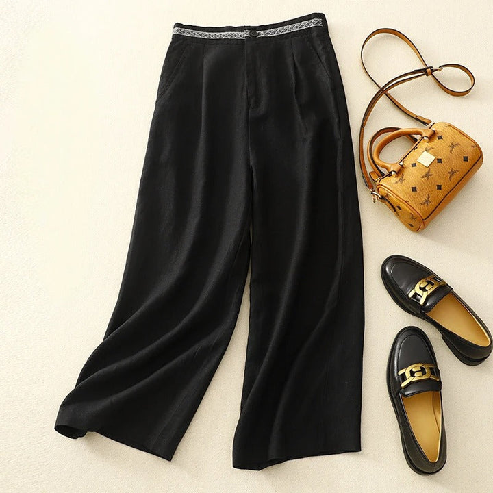 Flat lay of black linen pants with a patterned waistband, styled with a handbag and loafers