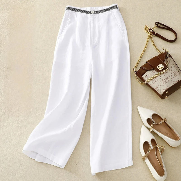 Front view of white linen pants with a patterned waistband, styled with a handbag and shoes