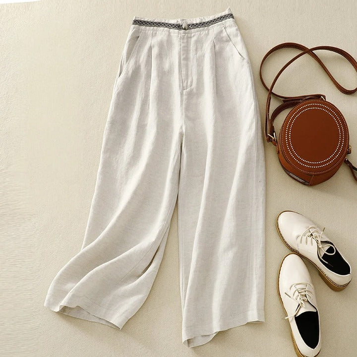 Flat lay of white linen pants with a patterned waistband, styled with a round handbag and white shoes