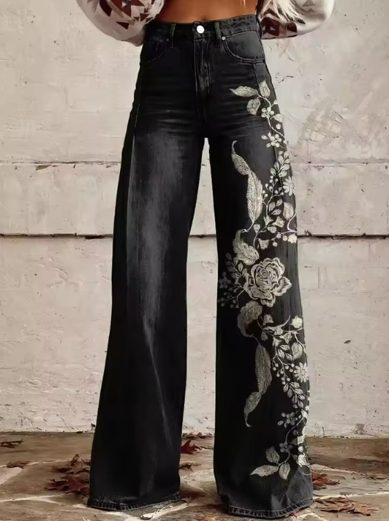 Front view, worn by model, of black high waisted wide leg boho vintage pants with white floral embroidery on right leg