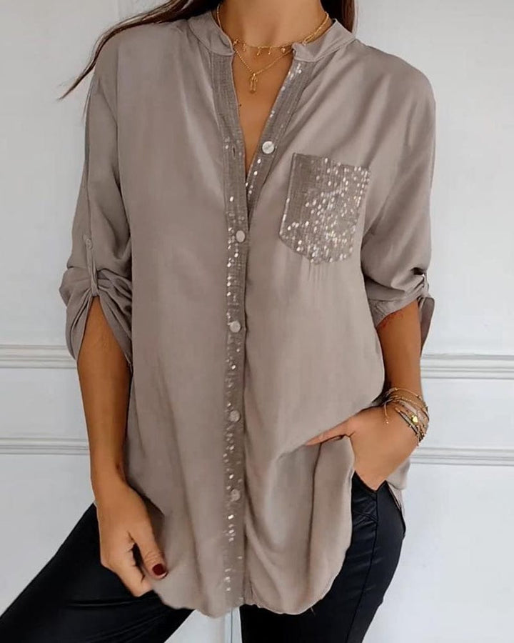 Front view of a model wearing a taupe button blouse with sequined placket and pocket, hands in pockets