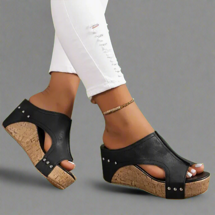 Worn by model, two feet in black elegant summer wedge sandals with studded cork-look soles, white ripped jeans