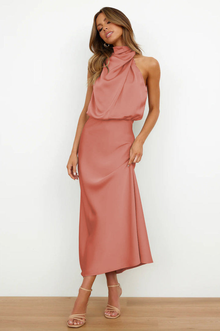 Front view, model wearing a long satin dress in dusty pink with a draped halter neckline and flowing skirt