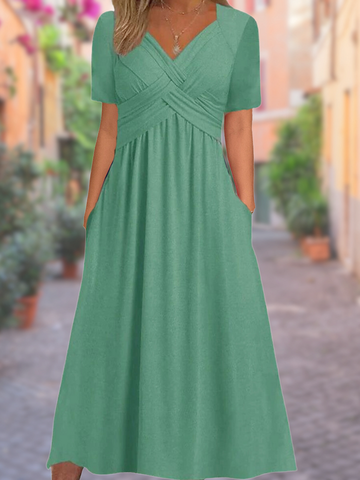 Front view of a green V-neck dress with short sleeves, a ruched bodice, and pockets, worn by a model