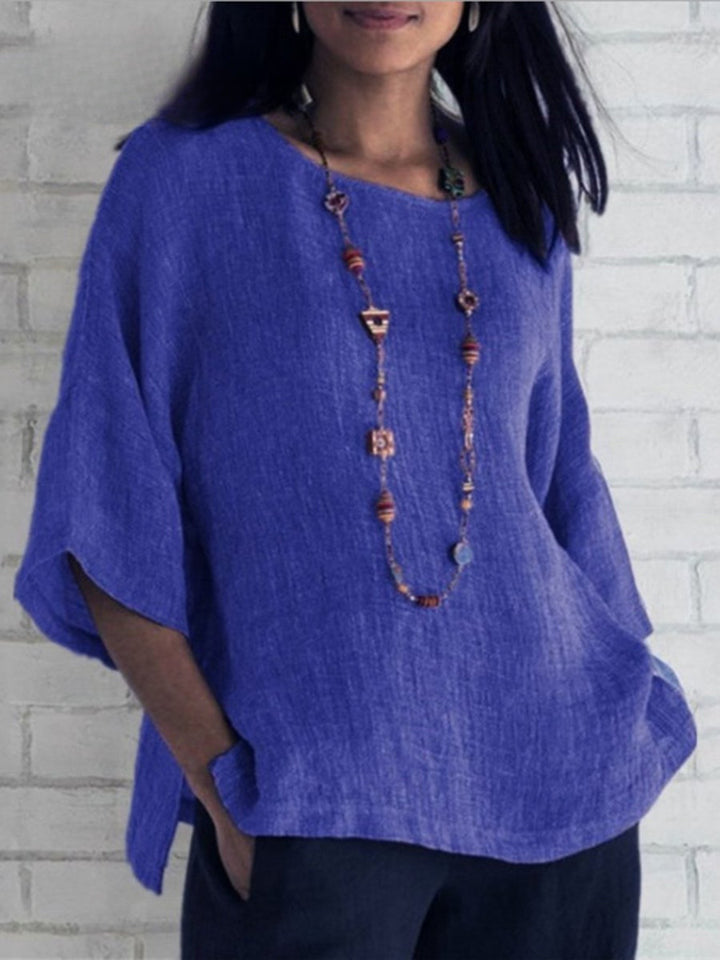 Front view of a model wearing a royal blue crewneck cotton linen shirt top with a long beaded necklace