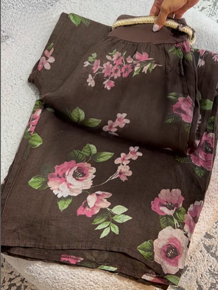 Flat lay of floral print cotton linen pants with a hand holding the braided drawstring waist, alternate angle