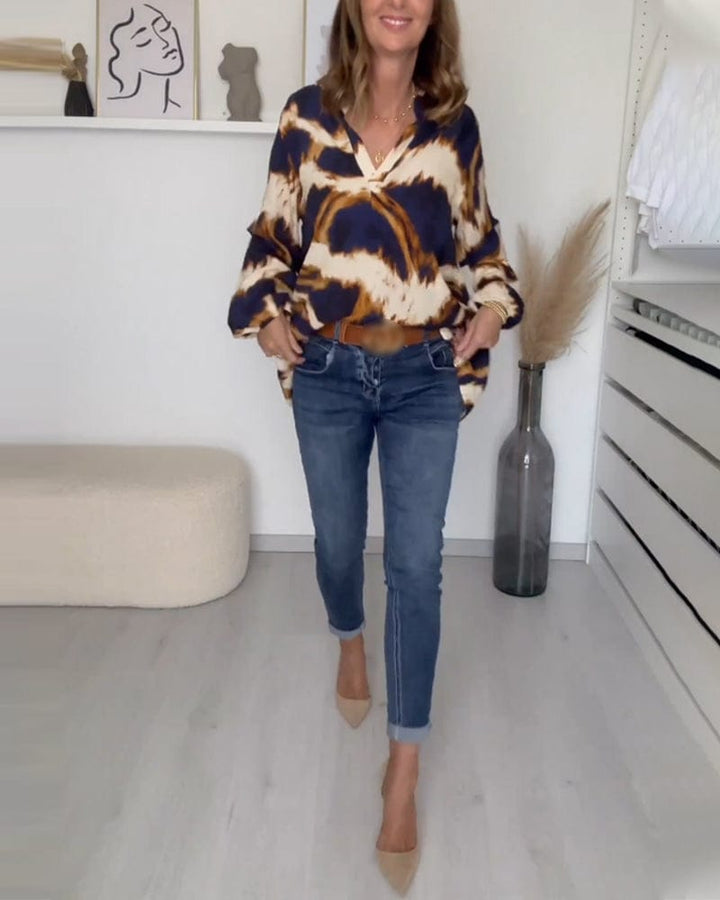Front view of a woman wearing a casual printed V-neck blouse tucked into blue jeans and nude heels