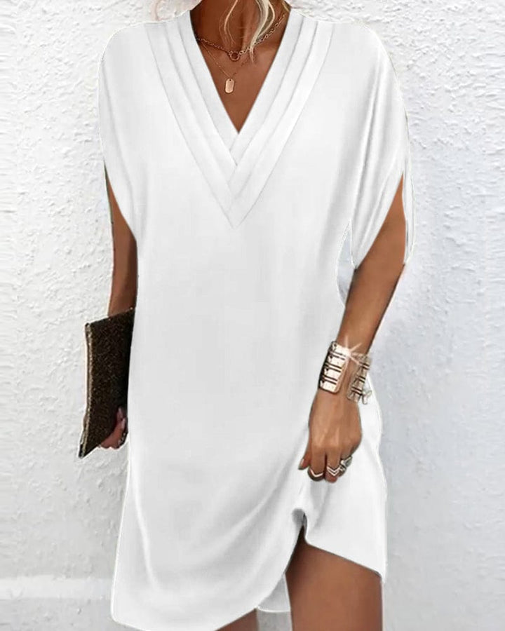 Front view of a model wearing a white V neck mini dress with batwing sleeves and a brown clutch bag