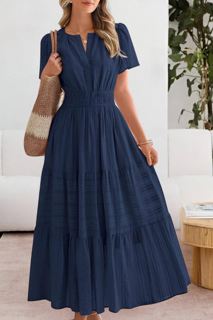 Front view of a woman in a navy Boho Breeze summer dress with a smocked waist and tiered skirt, carrying a tote bag