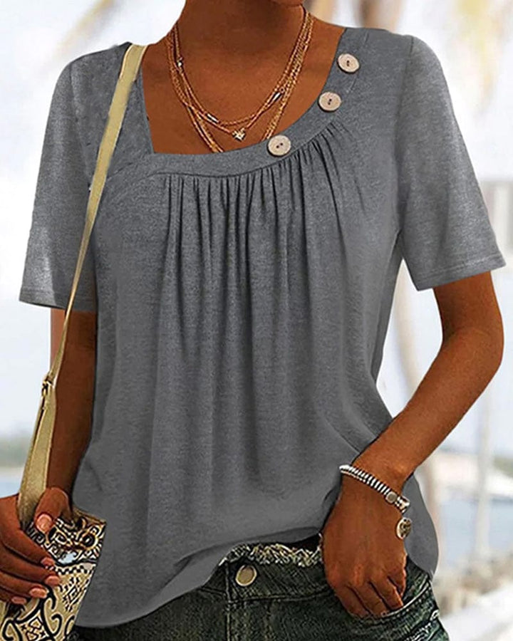 Front view of a model wearing a grey short sleeve blouse with a square neck and decorative buttons