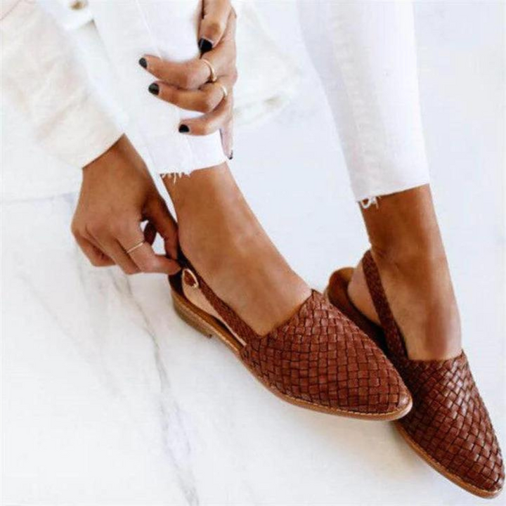 Close up of brown woven flat sandals with slingback straps, worn by model with white pants