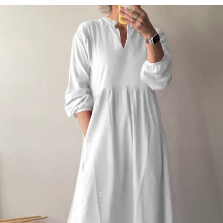 Front view, model wearing a white cotton dress with pockets, long sleeves, and a v-neckline