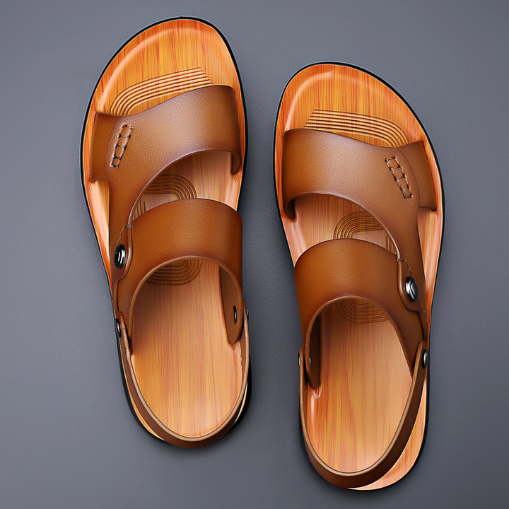 Front view of a pair of tan leather sandals with a wood-look sole on a grey background