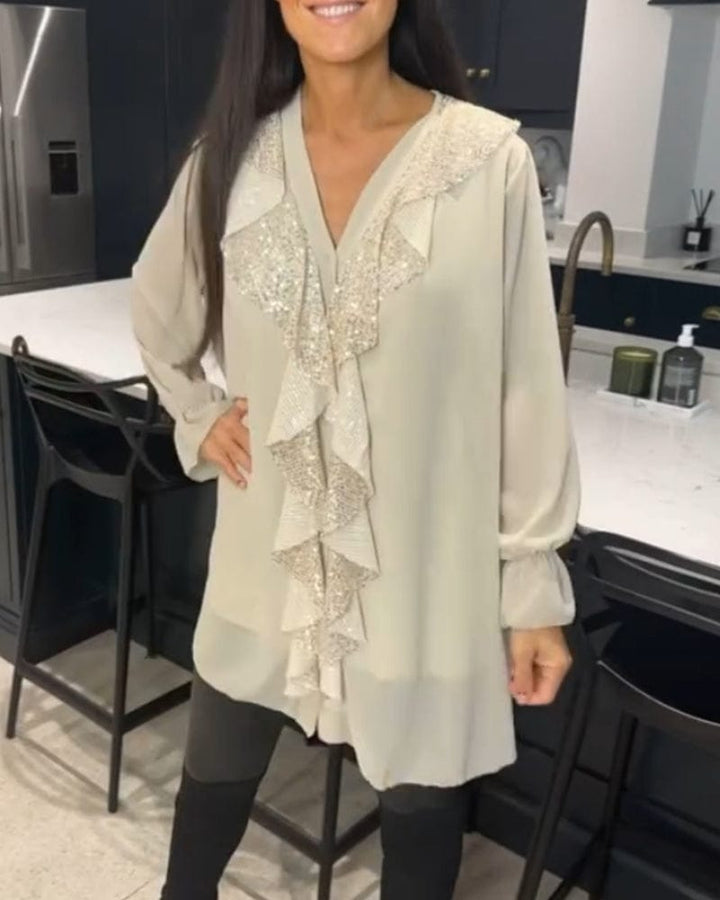Front view of a woman wearing a beige ruffled blouse with sequin detail and black leggings