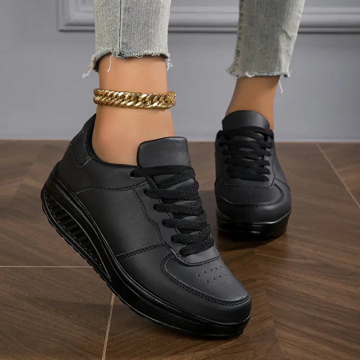 Three quarter view, worn by model, of black Myrtle comfort sneakers with thick black soles and a gold ankle bracelet