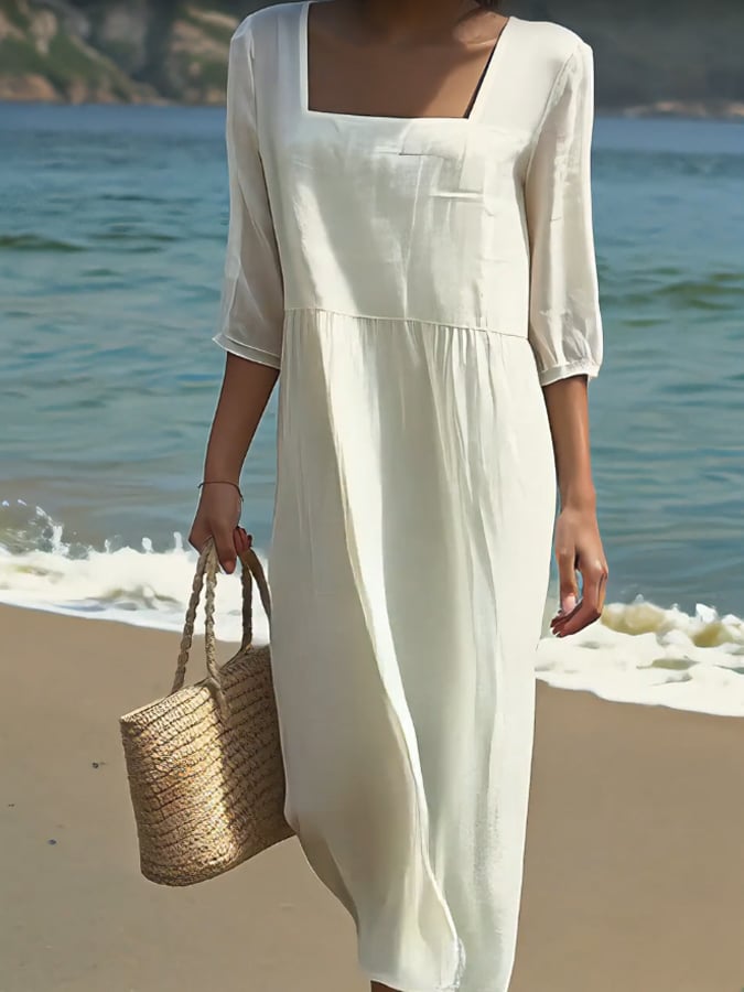 Close up of a model wearing a white cotton linen casual dress with a square neckline and a woven bag on a beach