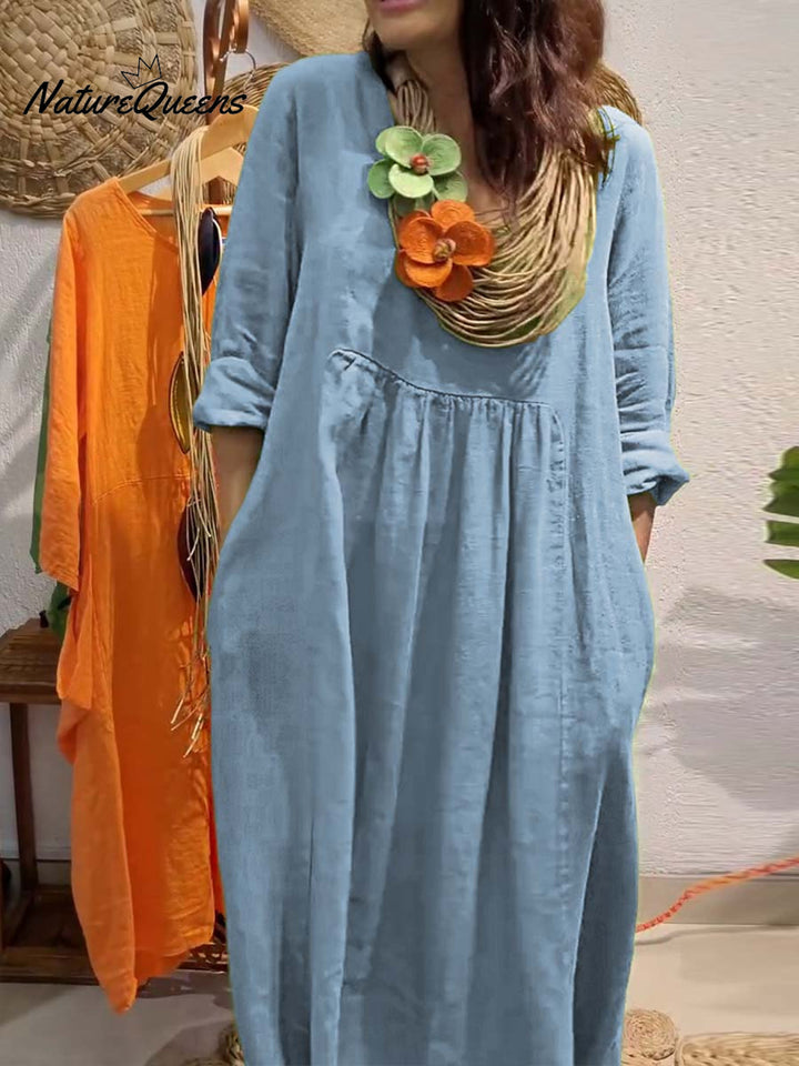 Front view, model wearing a blue V-neck cotton linen dress with 3/4 sleeves, large pockets and a statement necklace
