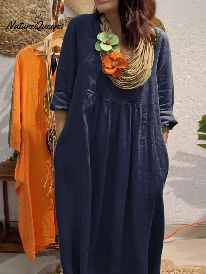 Front view, model wearing a navy V-neck cotton linen dress with 3/4 sleeves, large pockets and a statement necklace