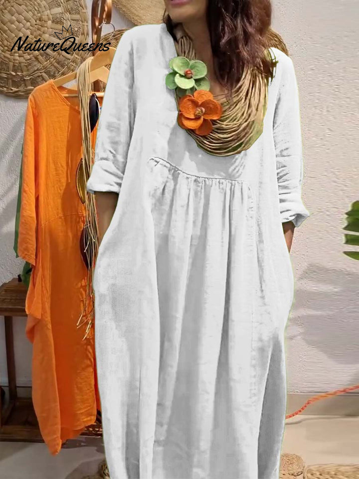 Side view, model wearing a white V-neck cotton linen dress with 3/4 sleeves, large pockets and a statement necklace