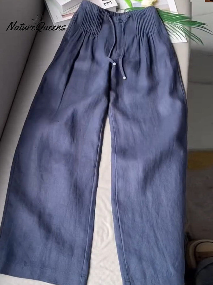 Front view of blue solid colour pleated drawstring wide leg pants with a button and white tie on a flat surface