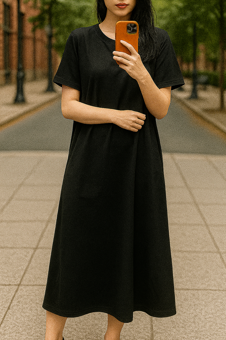 Front view, worn by model, of a black flowing maxi dress with short sleeves, holding an orange phone