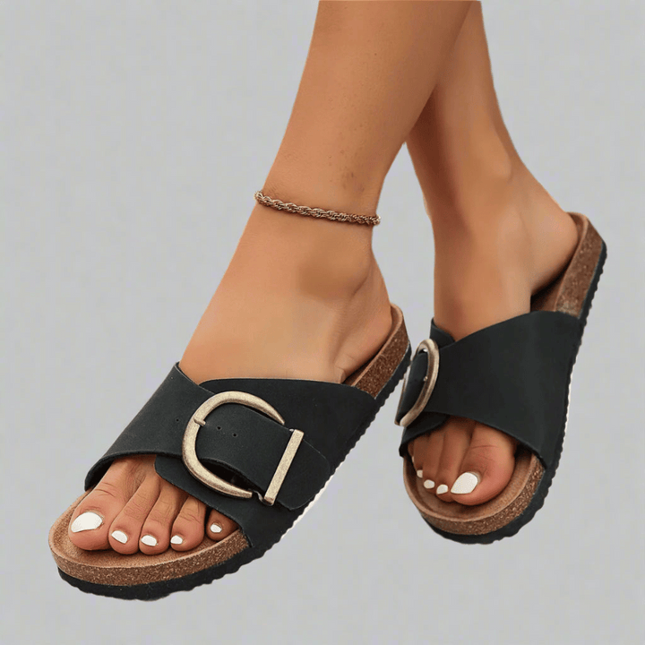 Siena vegan sandals worn by model, a pair of black slides with a gold buckle and cork sole, white painted toenails