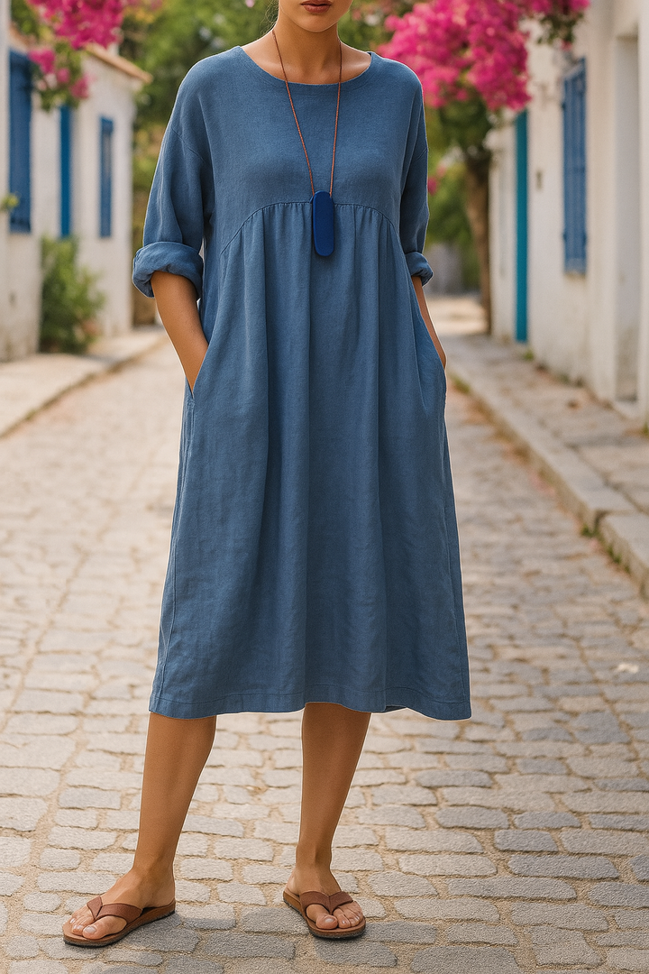 Front close up of a model wearing a blue round neck 3/4 sleeve boho dress with pockets and a long necklace