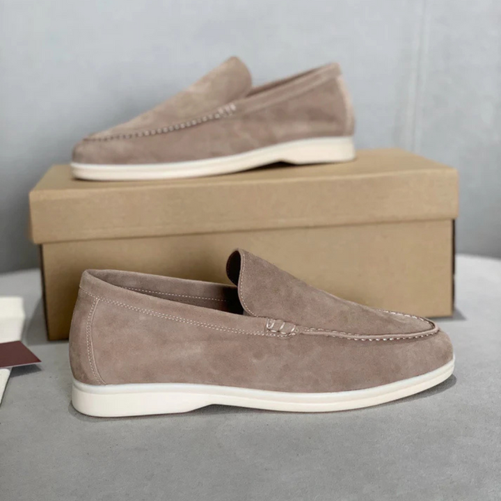 Side view of two pairs of tan suede loafers with white soles, one in front of a shoe box
