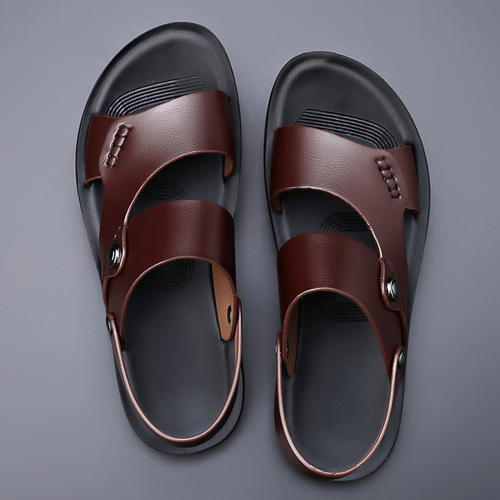 Top view of a pair of brown leather sandals with a dark sole on a grey background