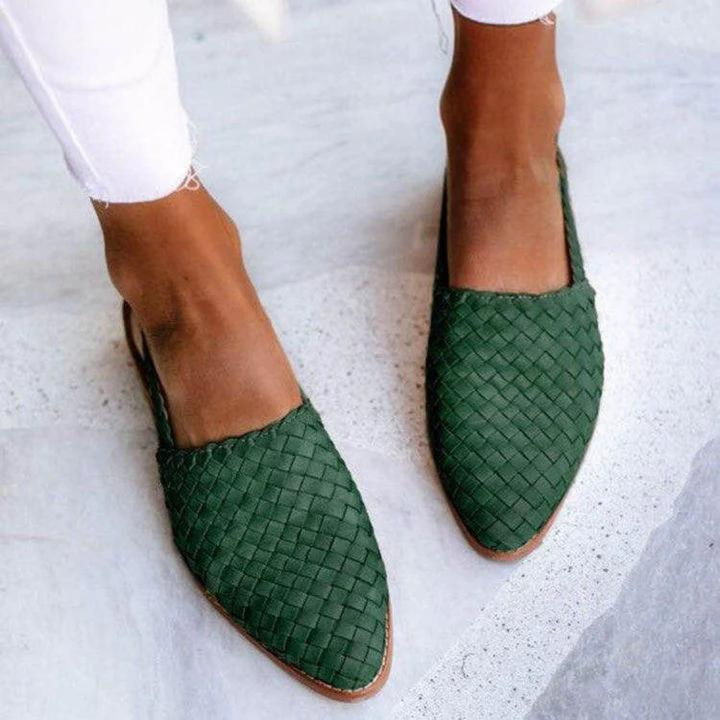 Top view of two feet in green woven flat sandals with slingback straps, worn with white pants