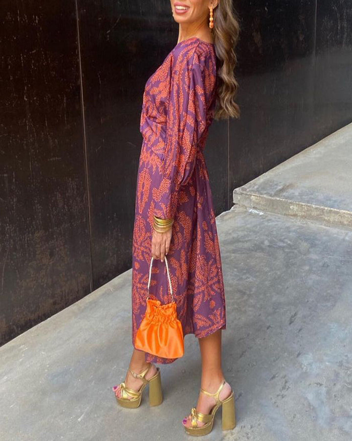 Side view, model wears a purple and orange patterned lightweight flowy summer dress with an orange clutch