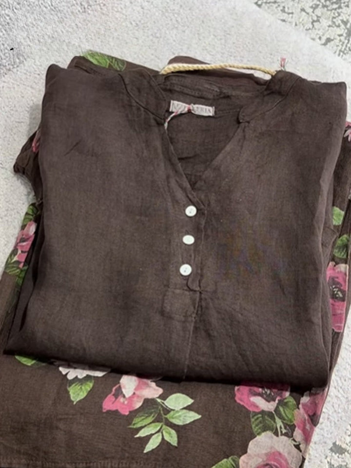 Flat lay of a folded brown cotton linen shirt with a v-neck and white buttons over a floral pattern