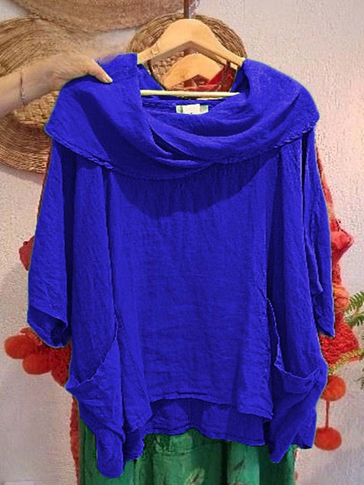Front view of a blue linen pocket top with a draped neck and 3/4 sleeves, held on a wooden hanger