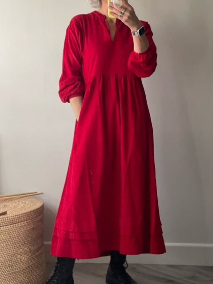 Front view, model wearing a red cotton dress with pockets, long sleeves, and a v-neckline