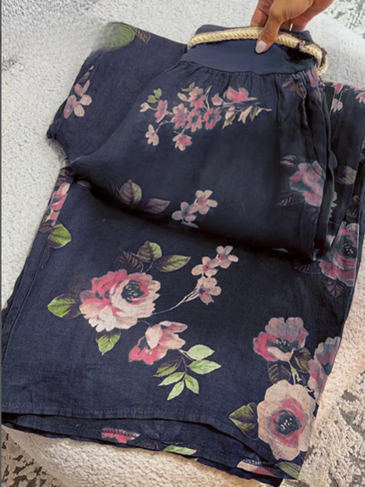 Flat lay of folded floral print cotton linen pants with a hand holding the braided drawstring waist