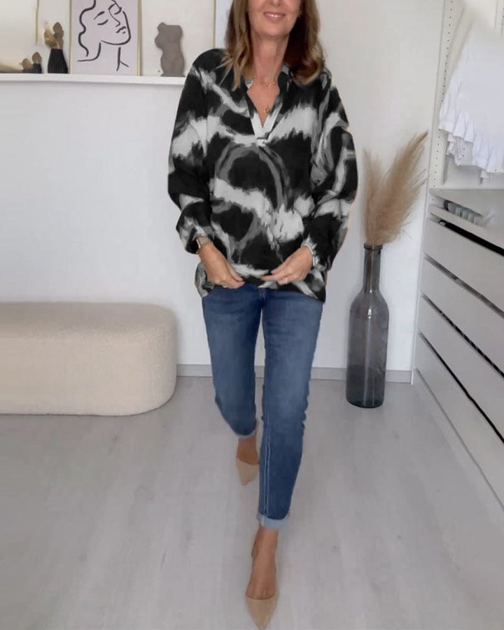 Front view of a woman adjusting her casual printed V-neck blouse, untucked, with cuffed blue jeans and nude heels